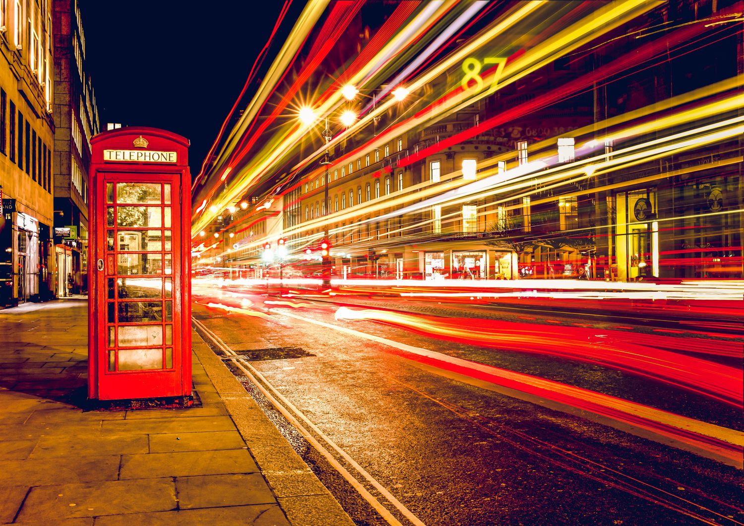 A red London telephone box at night with light trails from passing traffic