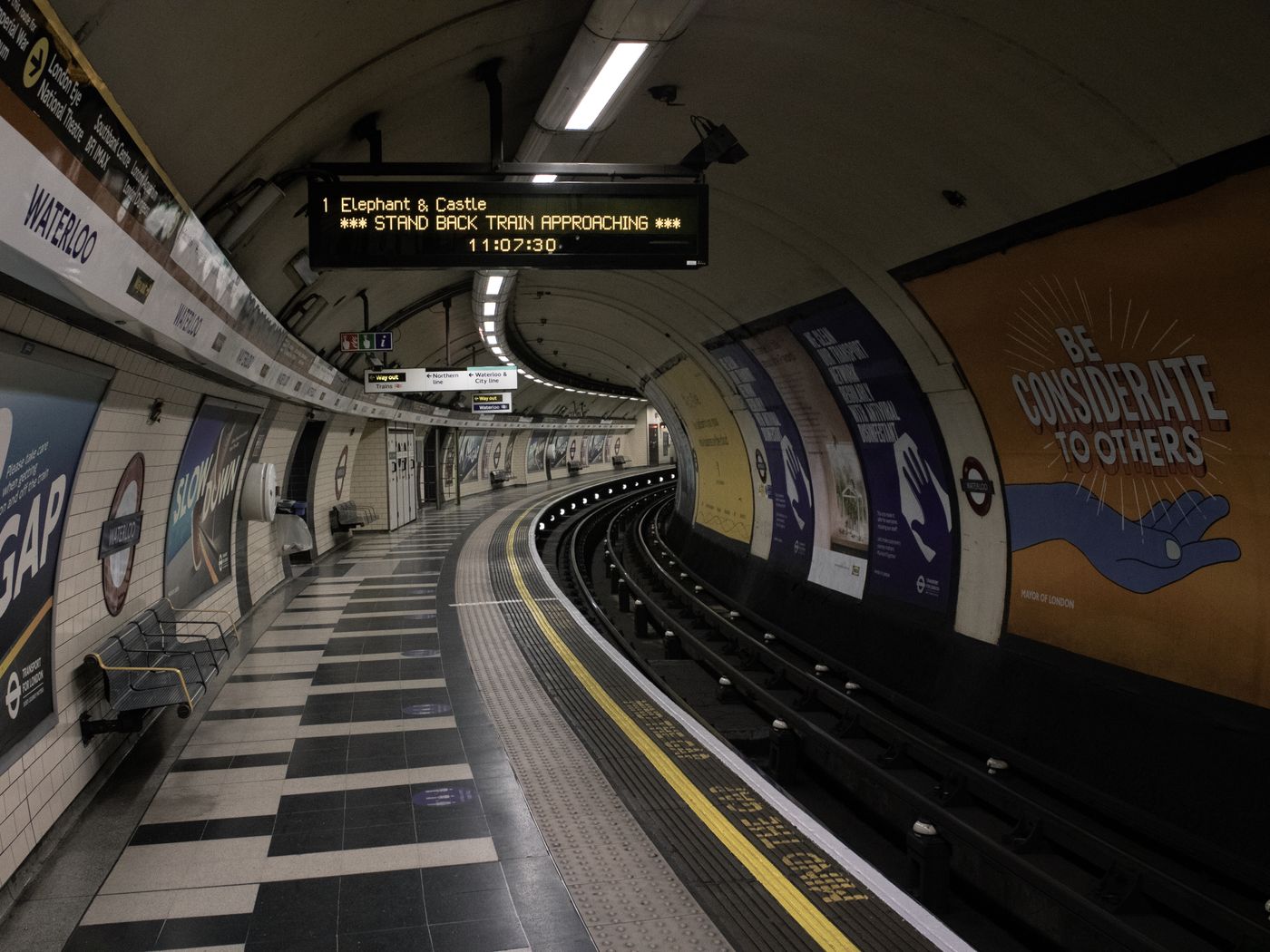 An empty London Underground platform lined with colourful advertisements