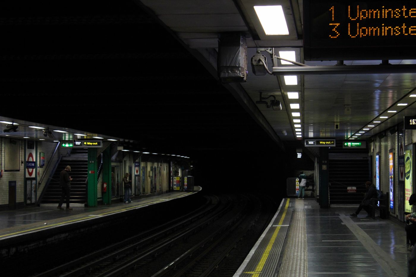 A dimly lit London Underground platform at night with passengers waiting